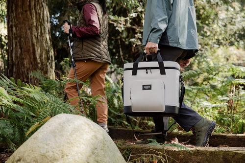 two people walking through the woods with a 30 can igloo trailmate soft cooler