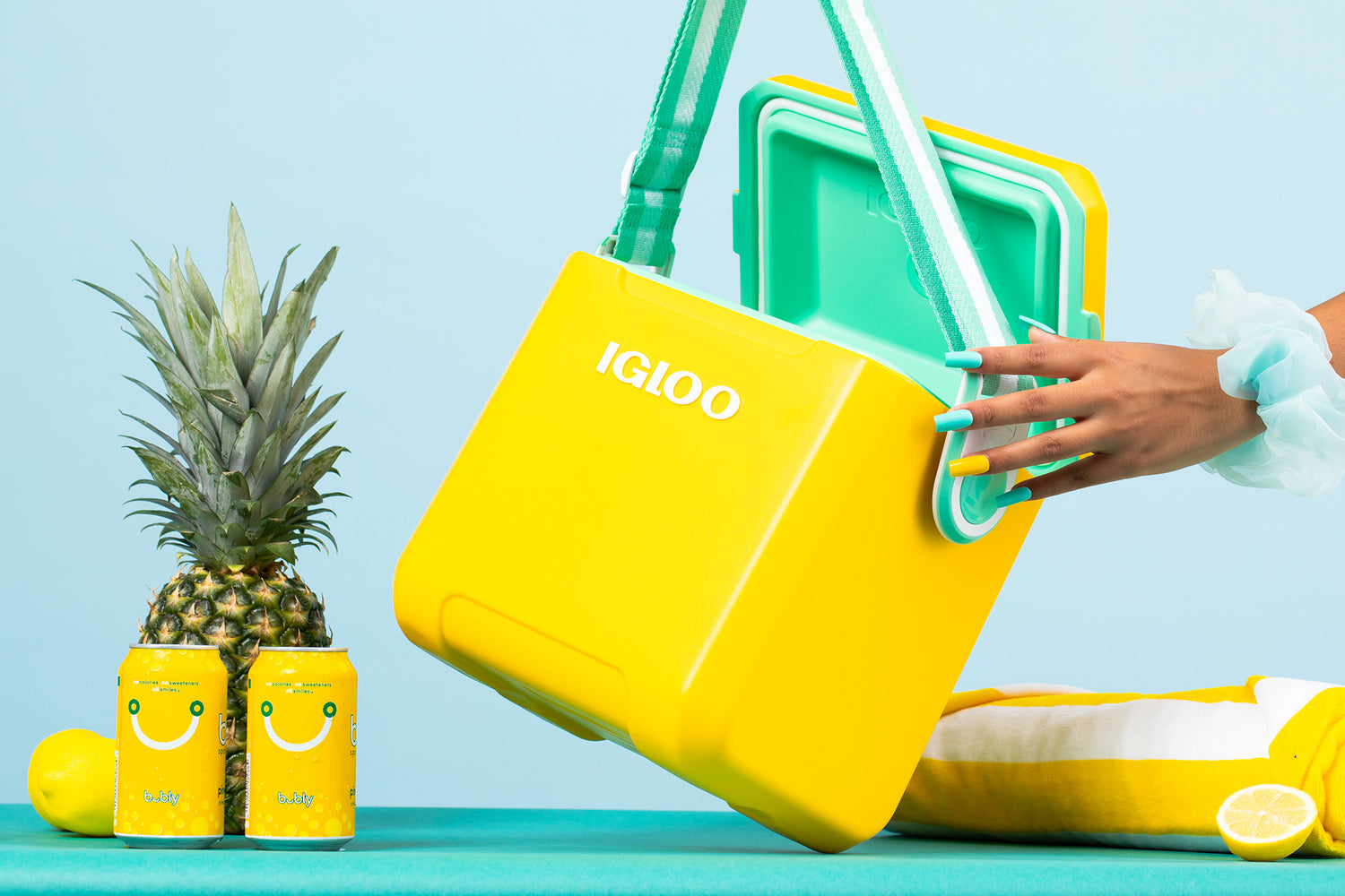 Yellow Igloo Tag Along Too Cooler next to pineapple, yellow soda cans, and yellow towel