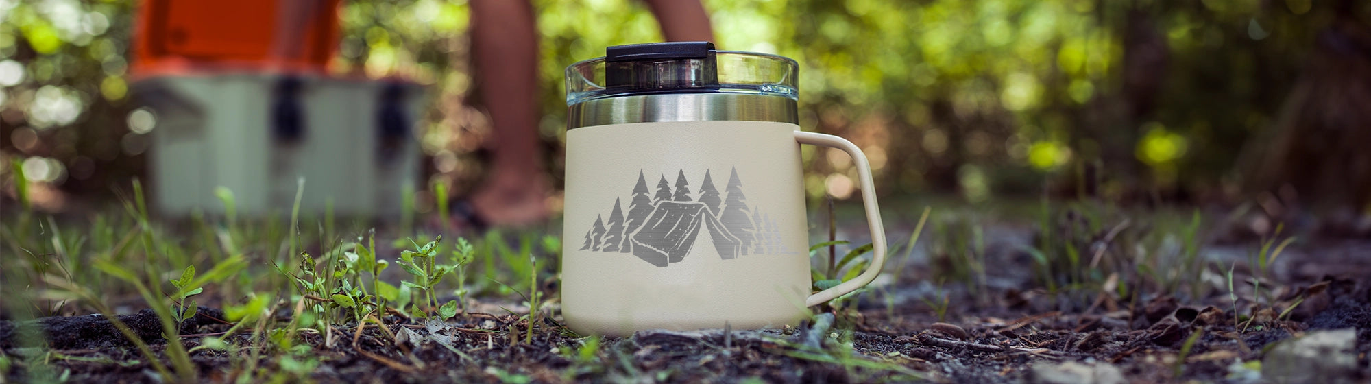 coffee mug in a camp setting with a custom laser engraving of a tent