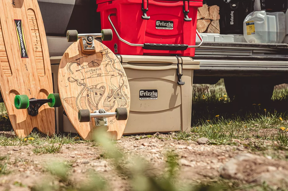 Red Grizzly cooler sits on top of larger tan Grizzly cooler next to wooden longboards and a van