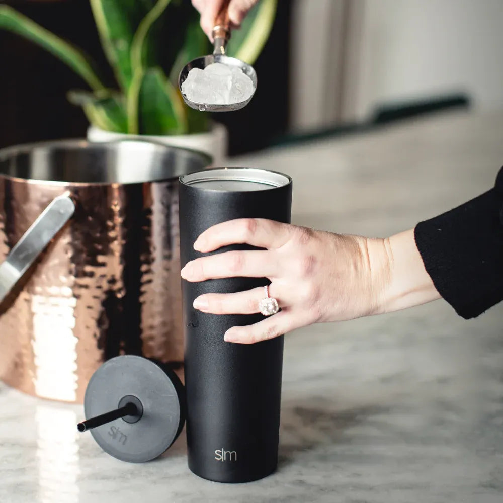 Woman putting ice into Simple Modern 20 oz classic tumbler with straw lid.