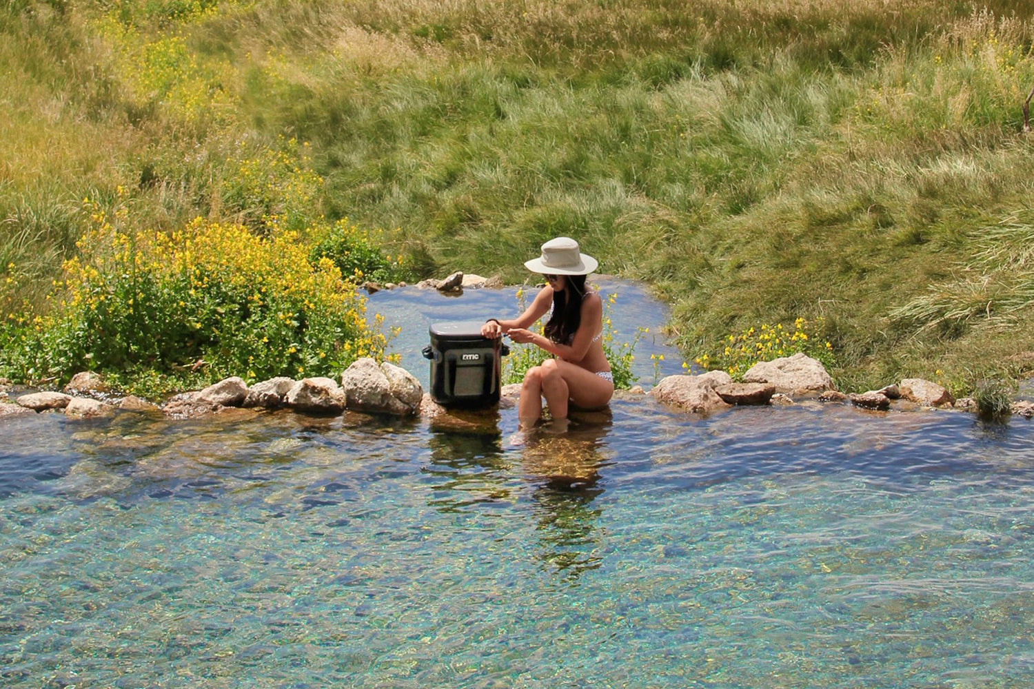 Woman sitting outside in water hole with RTIC soft cooler bag