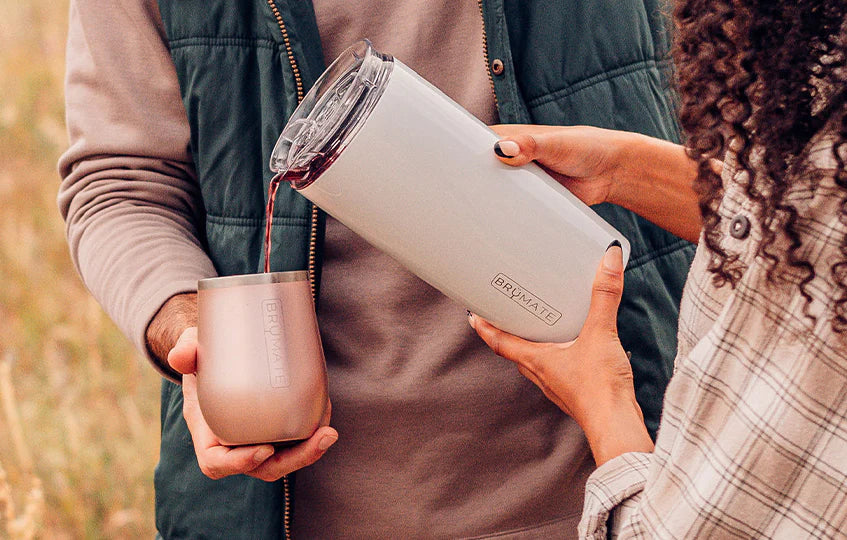 Woman pouring wine out of white Brumate Togosa bottle chiller and pitcher into rose gold Brumate wine tumbler