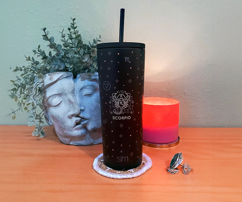 custom zodiac design on a straw lid simple modern tumbler. Tabletop scene with face planter and candle.