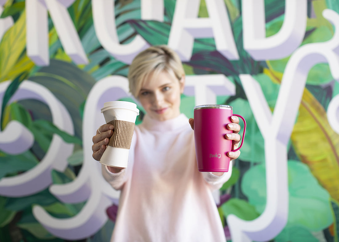 Woman holding crumpled cardboard coffee cup in right hand and holding pink Swig mug with handle in left hand