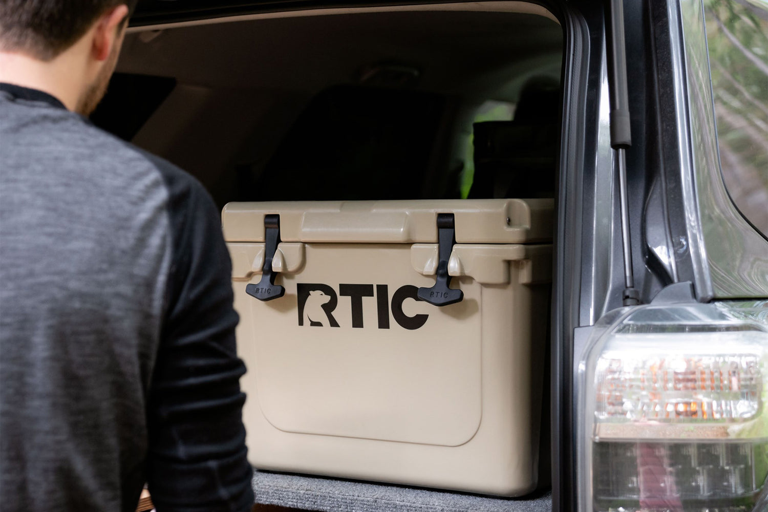 Man unloading trunk of car that has tan RTIC 20 quart cooler.