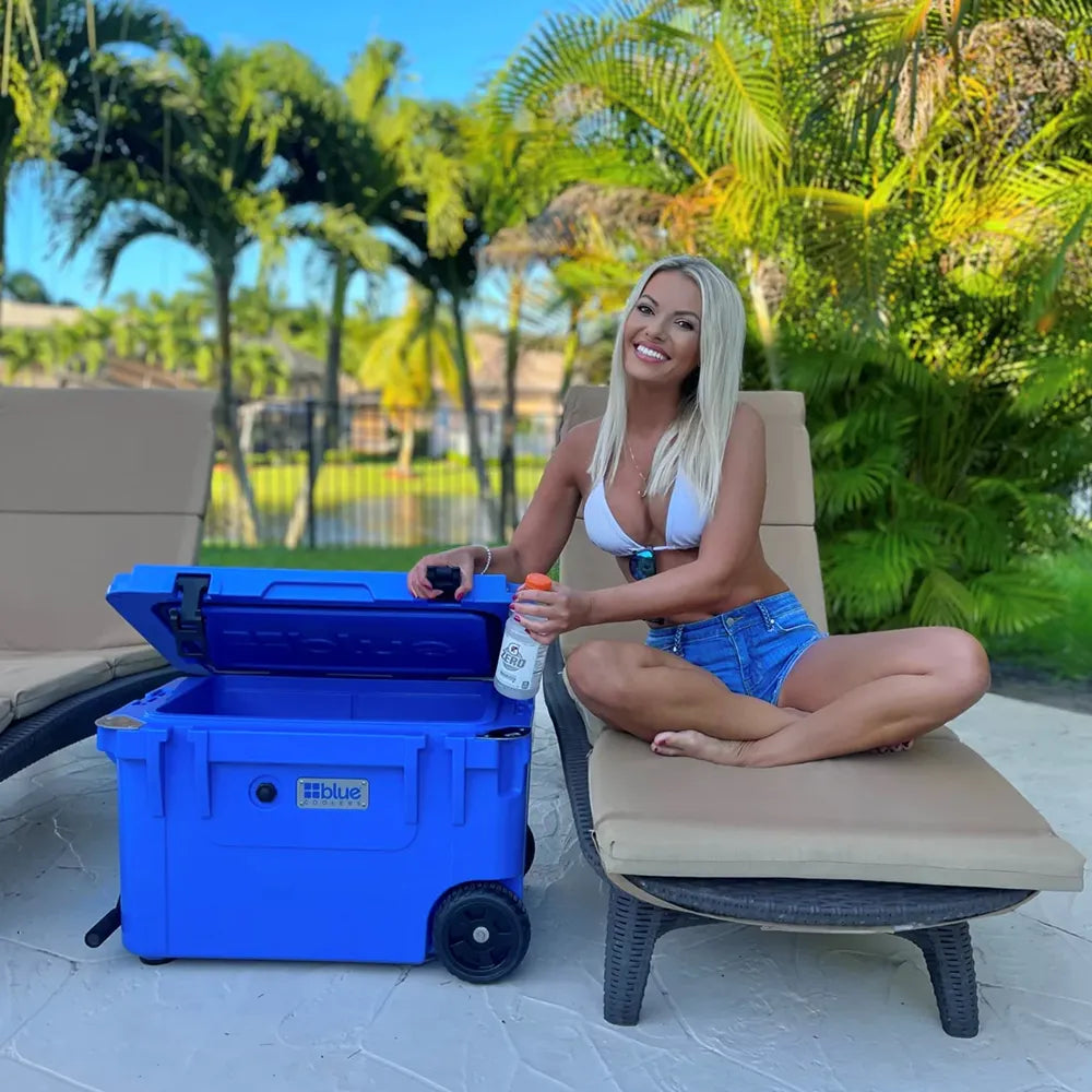 Woman by pool opening Blue Cooler 5 day 55 quart Cobalt Cooler with Wheels in blue.