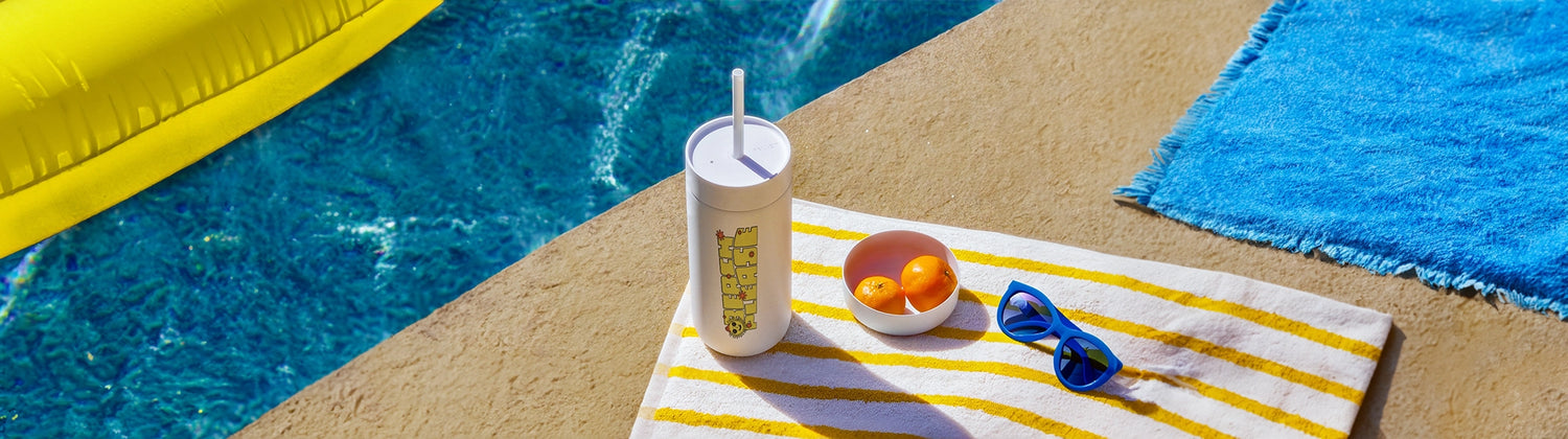summer themed custom printed tumbler with straw on towel by the pool