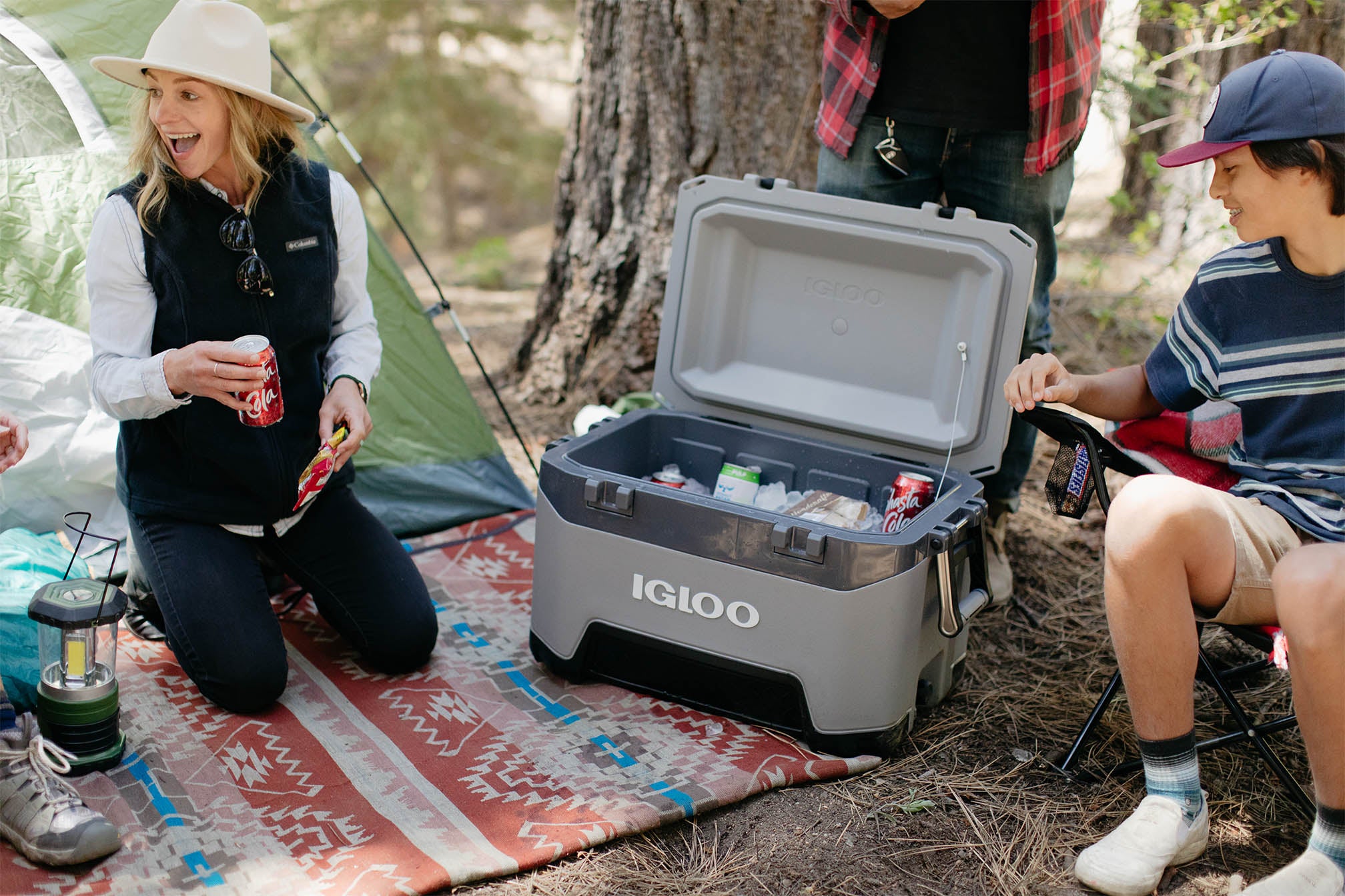 Family camping in woods with gray Igloo BMX 54 quart cooler