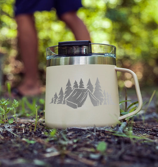 coffee mug in a camp setting with a custom laser engraving of a tent