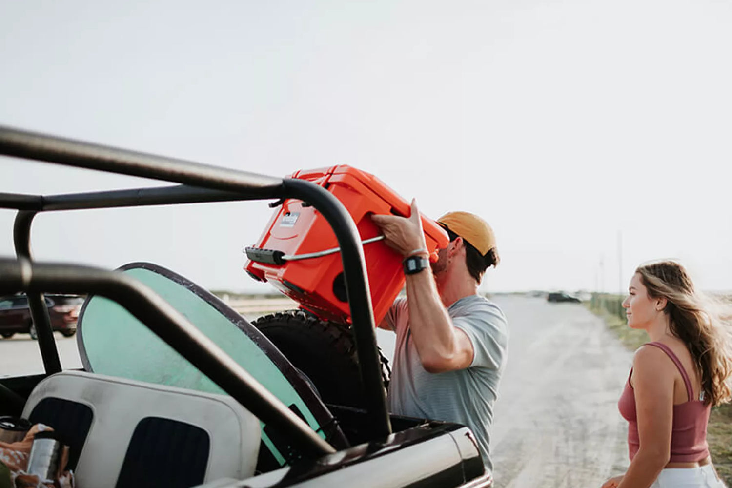 Man lifting orange Grizzly cooler out of jeep at the beach