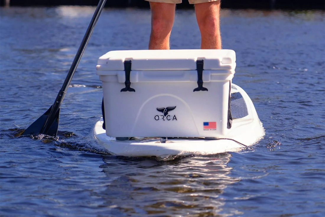 White Orca cooler sitting on paddle board on a lake