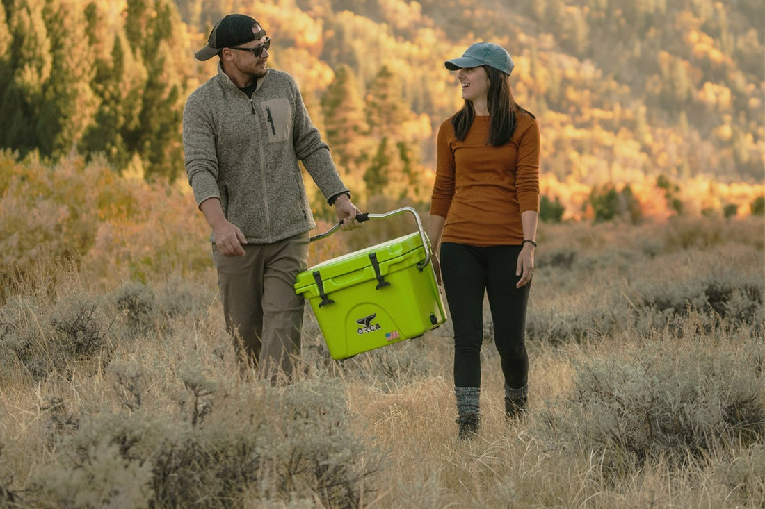Couple hiking through forest holding lime colored Orca cooler with handle