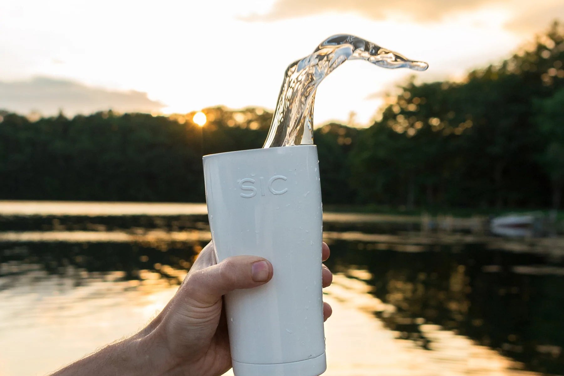 White SIC tumbler with water falling out of it with a lake in the background