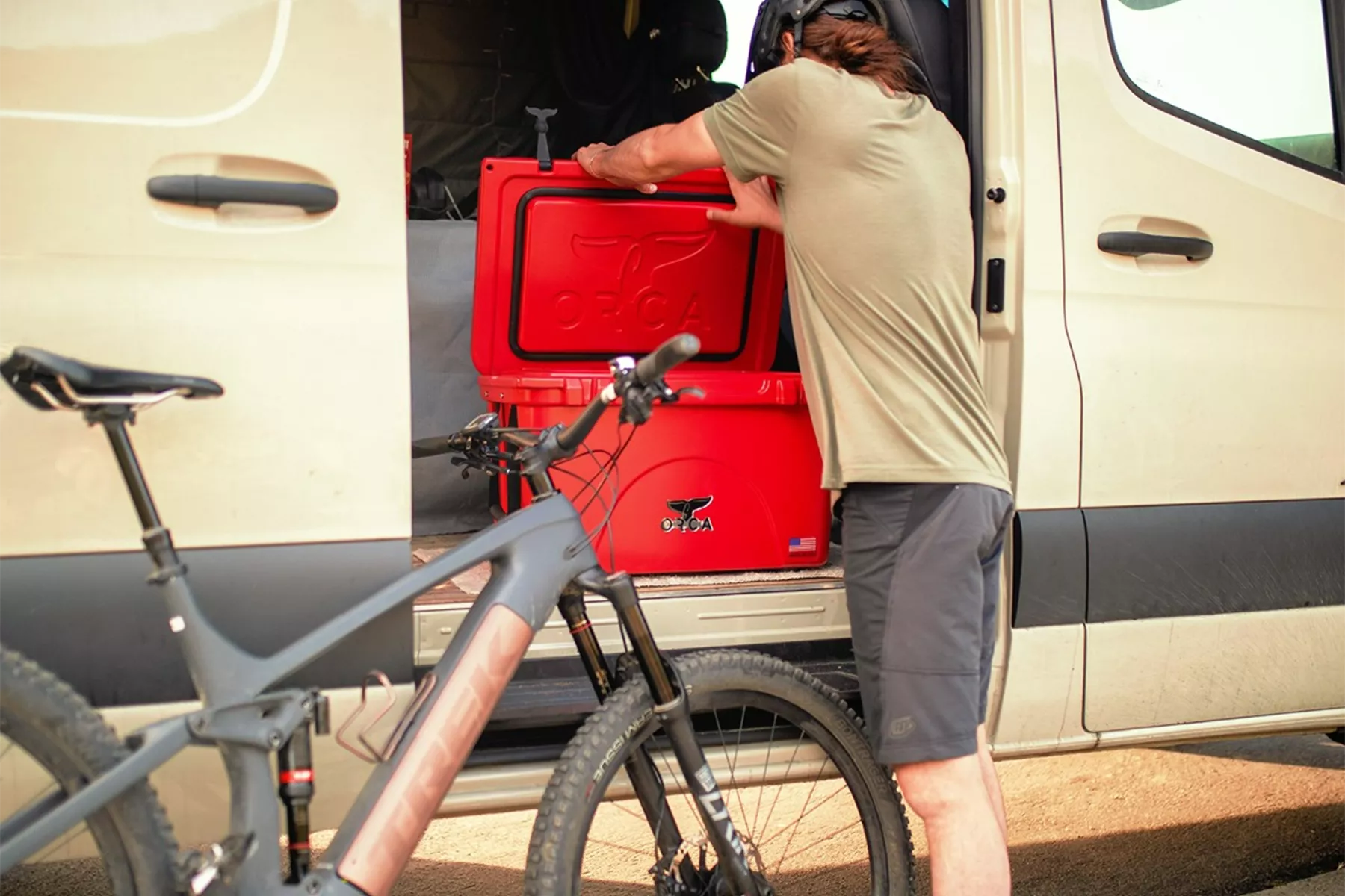 Man on a trip opening a red Orca cooler that is inside of a van
