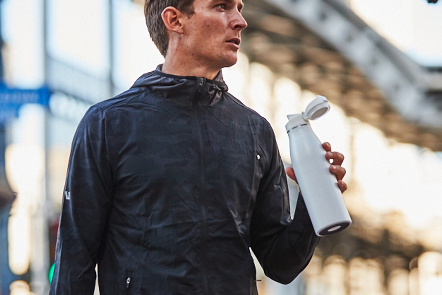 Man in black jacket drinking from white Takeya traveler mug with fliplock lid