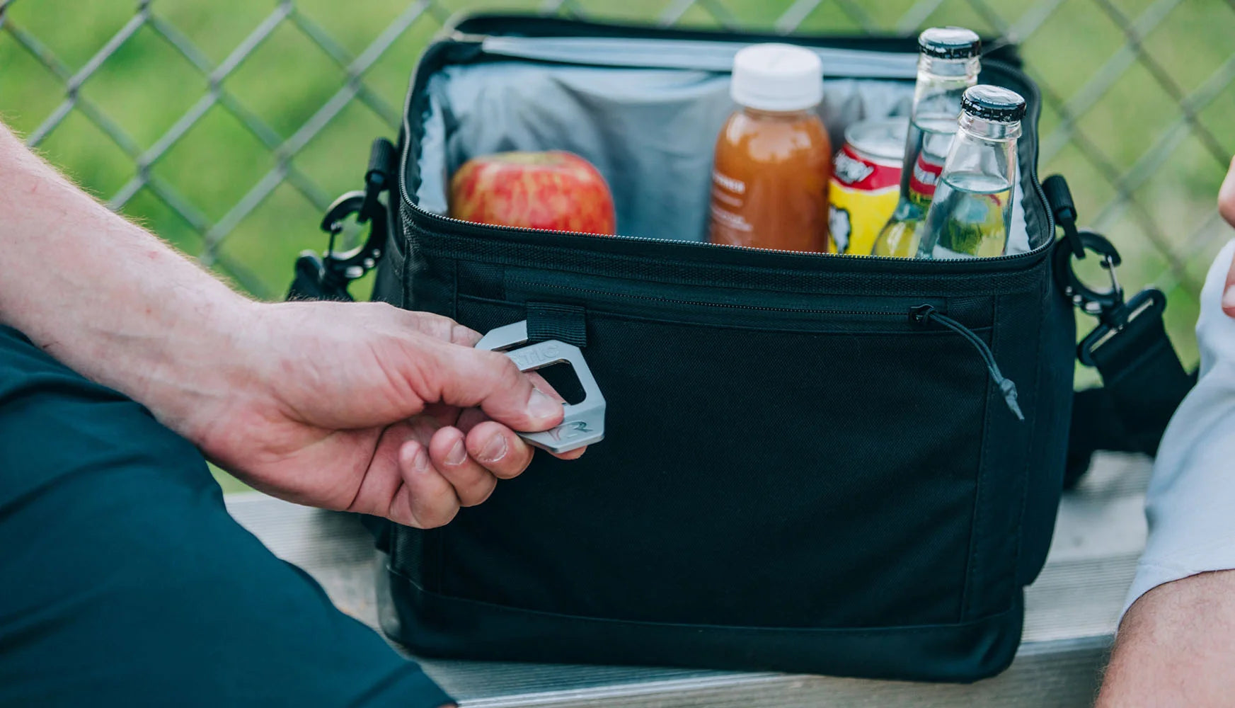 Man holding bottle opener attachment on black RTIC everyday cooler