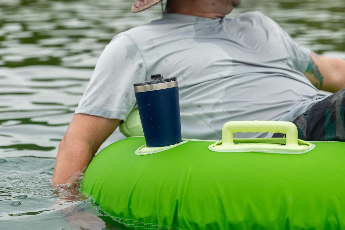 Man floating in green tube on the river with navy RTIC tumbler in cup holder of tube