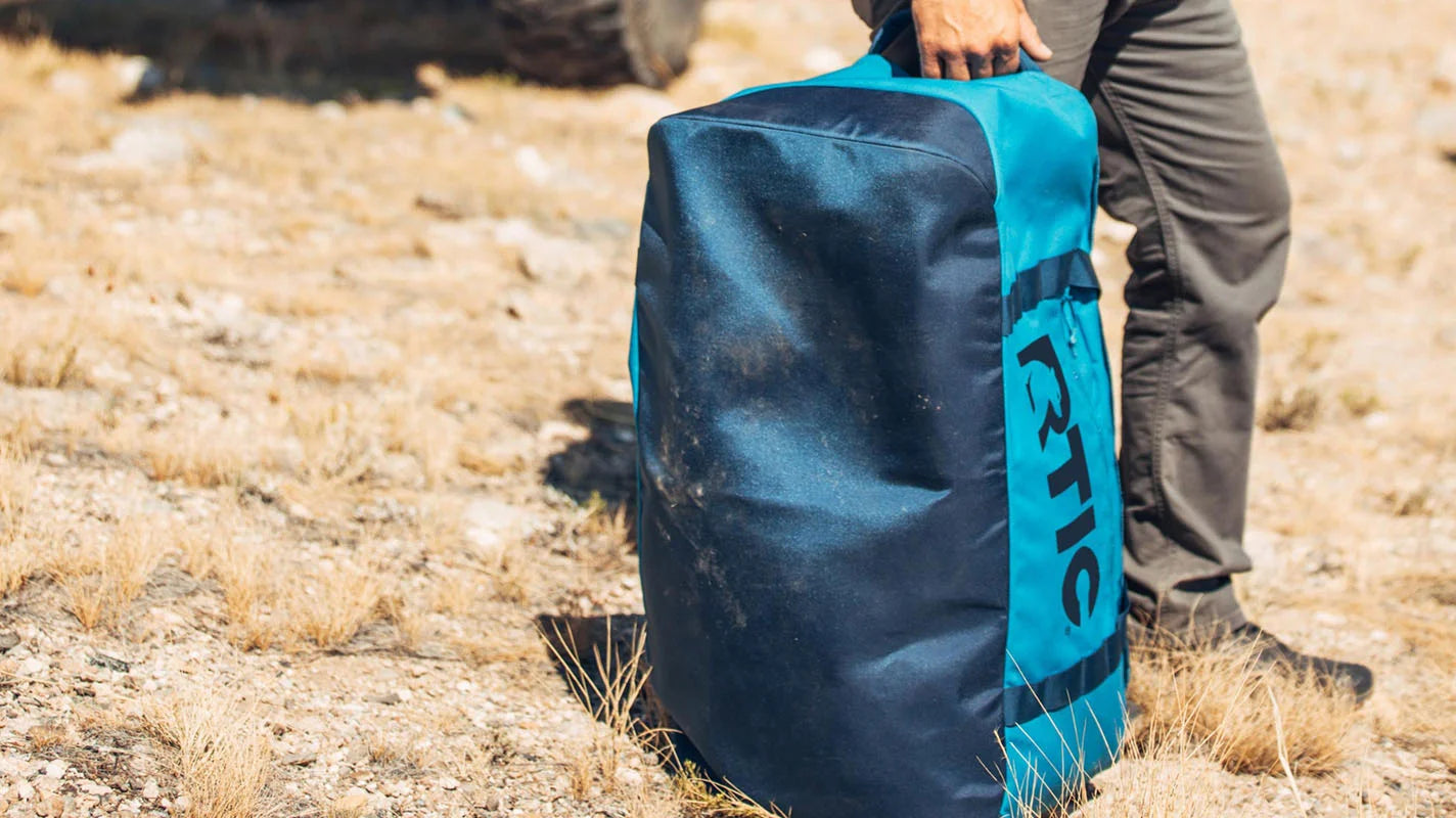 Blue RTIC Roadtrip duffle bag sitting upright in a field