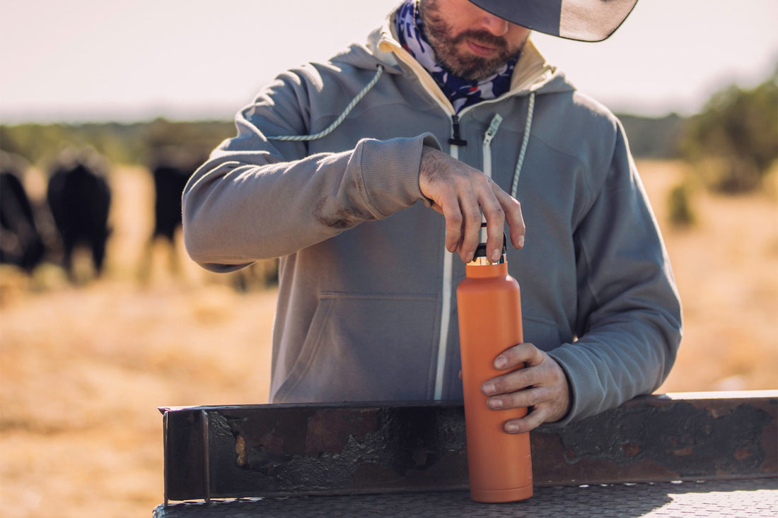 Rancher man holding orange RTIC water bottle.