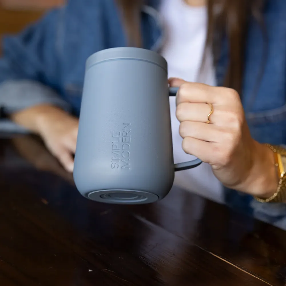 Person holding Simple Modern 12 oz Voyager Signature Mug at table.