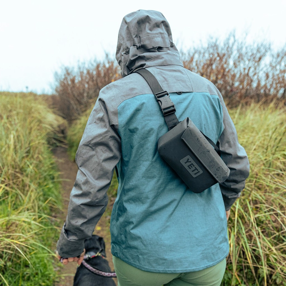 Person carrying Yeti 1 lt SideKick Dry® Waterproof Gear Case on their back as they walk their dog.