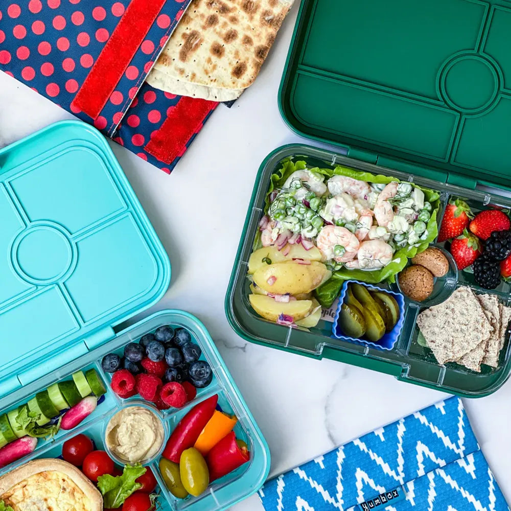 Two Yumbox Tapas 5 Compartment Bon Appetit Trays with packed lunches on a table.