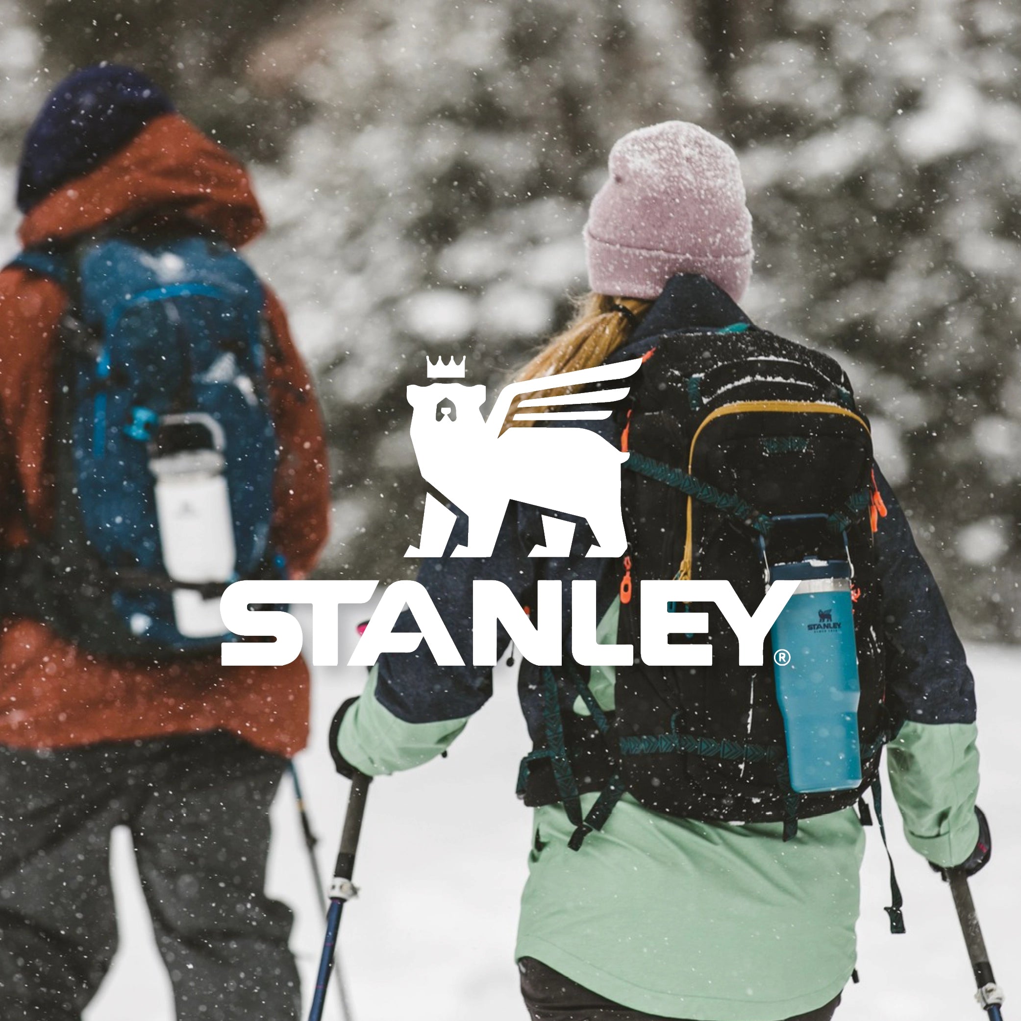 Couple hiking through the snow with Stanley IceFlow water bottles attached to their backpacks.