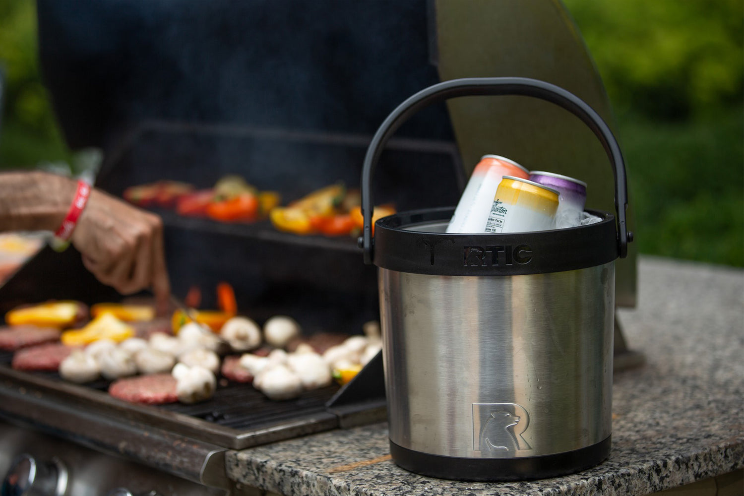 Man outside grilling with RTIC Ice Bucket sitting on shelf next to the grill