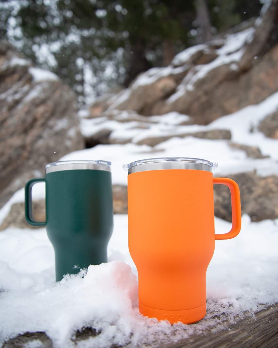 Green and orange orca traveler mugs sitting in snow