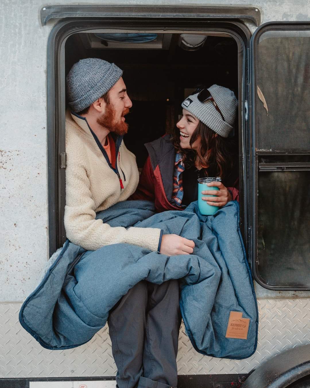 Man and woman sitting in camper holding blue Orca wine tumbler