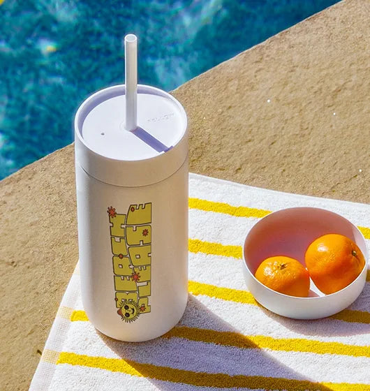 Custom straw tumbler with a sunshine print , sitting by a pool