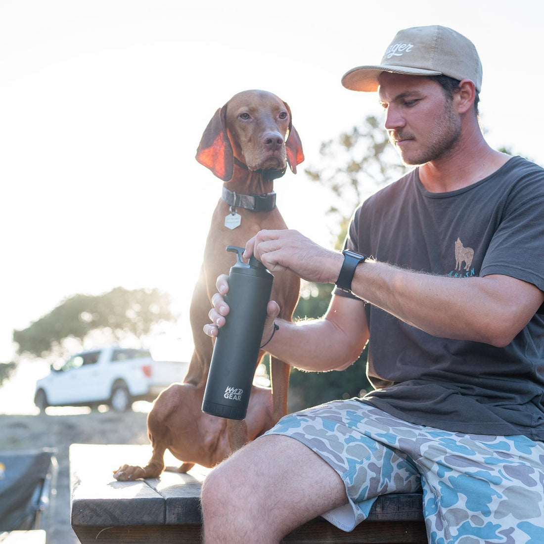 Man sitting with dog opening black Wyld Gear water bottle