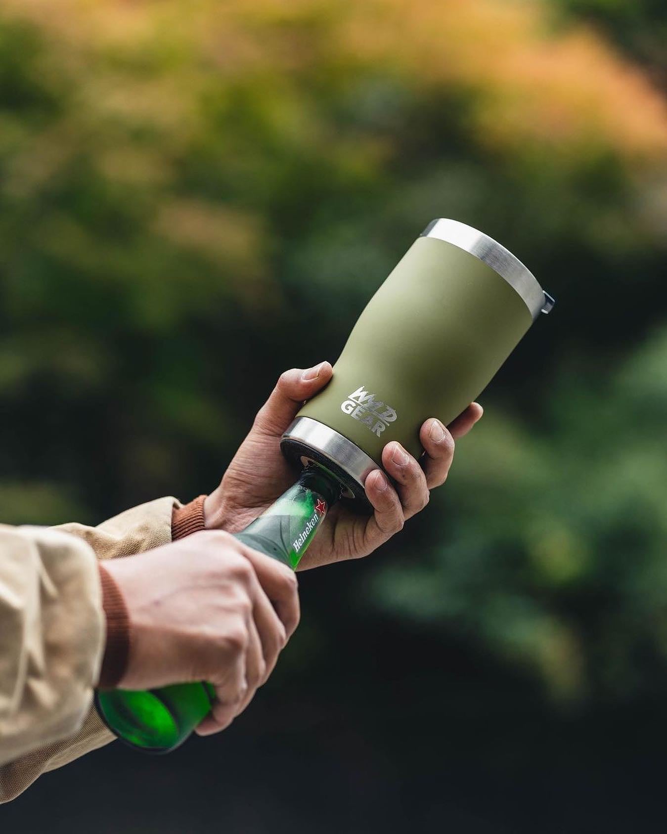 Man opening beer bottle with green Wyld Gear tumbler